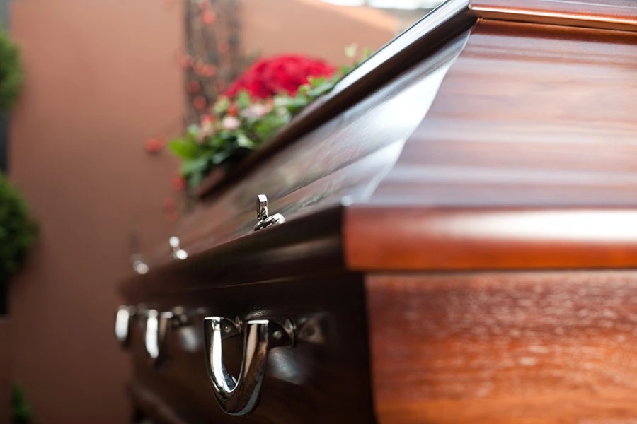 A polished wooden casket adorned with red flowers at a funeral setting.
