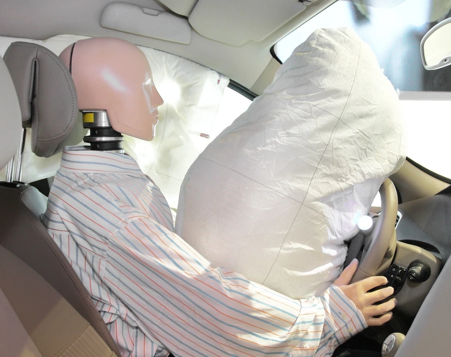 A crash test dummy sitting in the driver's seat of a vehicle with deployed airbags.