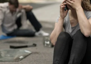 A distressed woman covering her face while making a phone call on a street near vehicle debris after an accident.