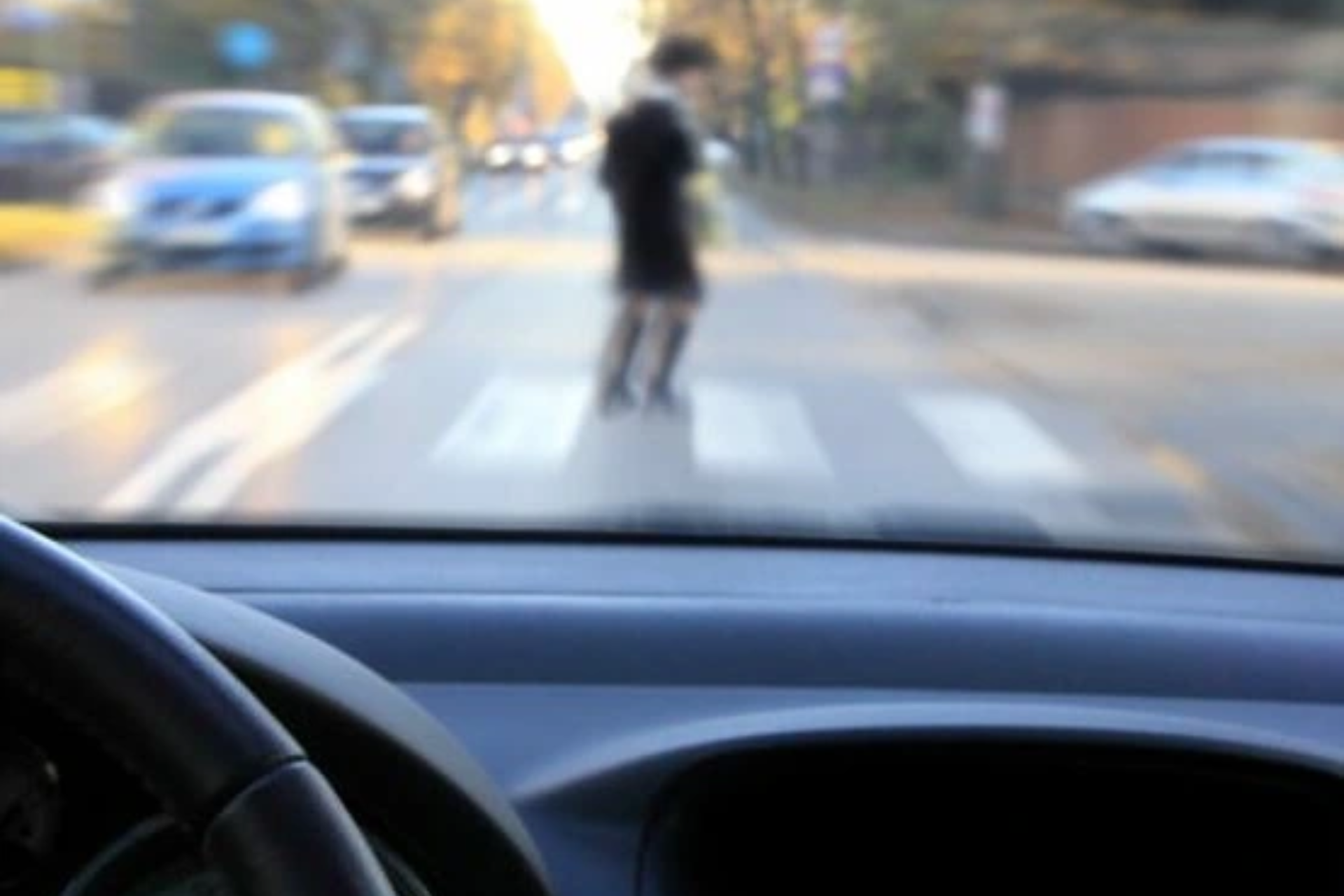 A driver's perspective from inside a car showing a blurred view of a pedestrian crossing the street at a crosswalk.