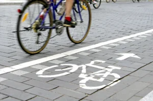 A cyclist riding along a paved city bike lane marked with a painted bicycle symbol and arrow.