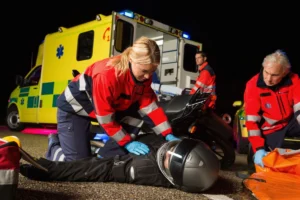 Paramedics responding to an injured motorcyclist lying on the ground at night in front of an ambulance.
