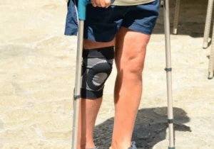 A person wearing a supportive knee brace standing with the aid of crutches.