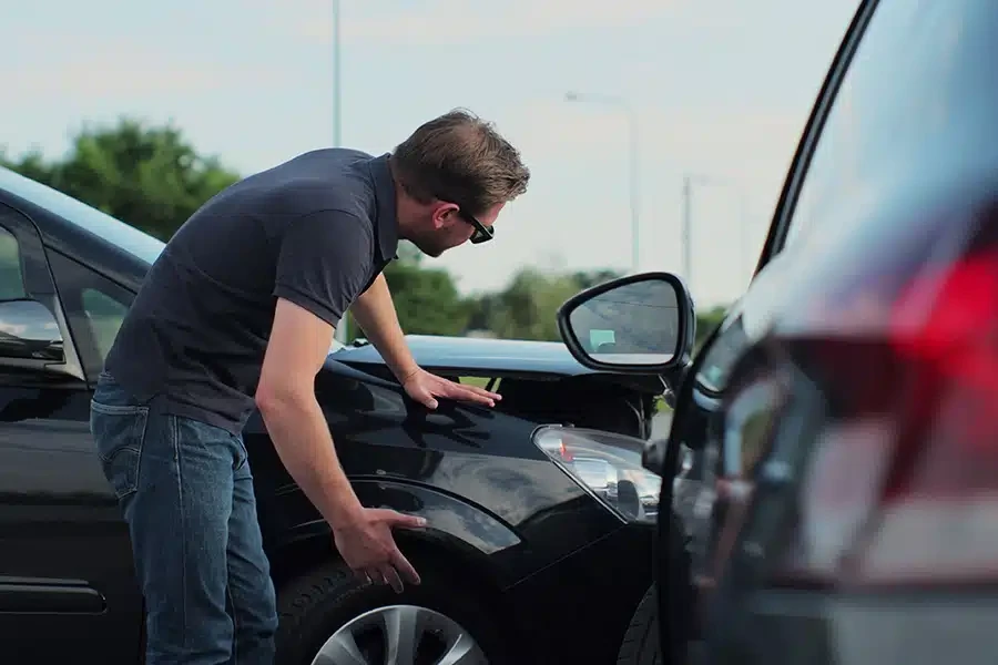 A man bending down to inspect the front fender damage after a minor car collision.