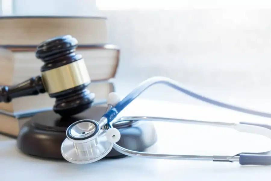 A stethoscope and a judge's gavel resting on a white desk next to law books.
