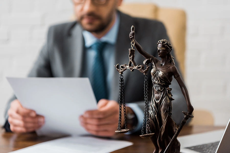 A lawyer reviewing documents at a desk behind a statue of Lady Justice.