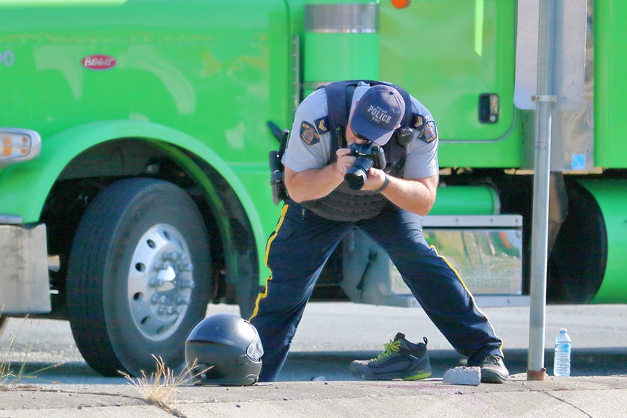 A police officer taking photos of evidence in front of a green semi-truck.