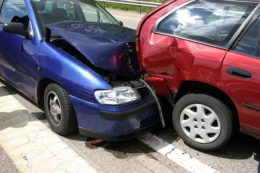 A blue car rear-ending a red hatchback on a road.