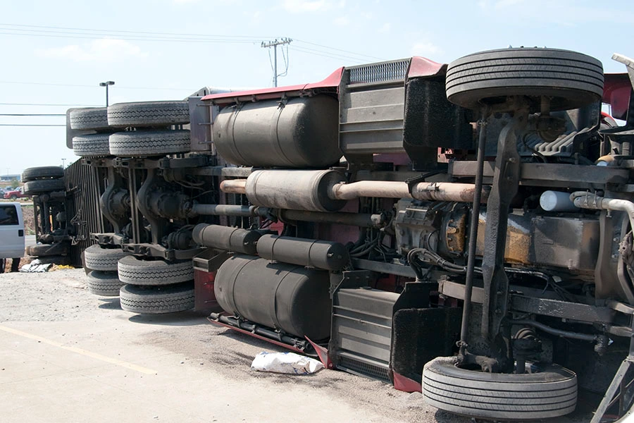 The undercarriage of a red semi-truck turned over on its side.