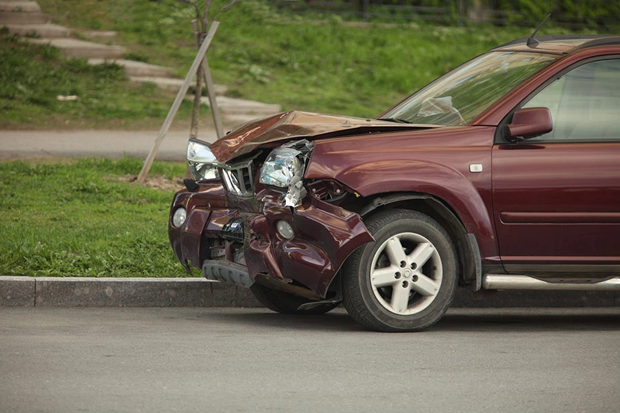 A maroon SUV with severe front-end damage from a collision, parked along a curb.