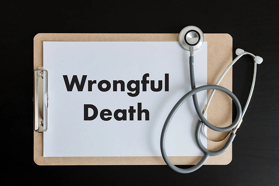 A wooden clipboard with a paper reading "Wrongful Death" next to a coiled stethoscope on a dark surface.