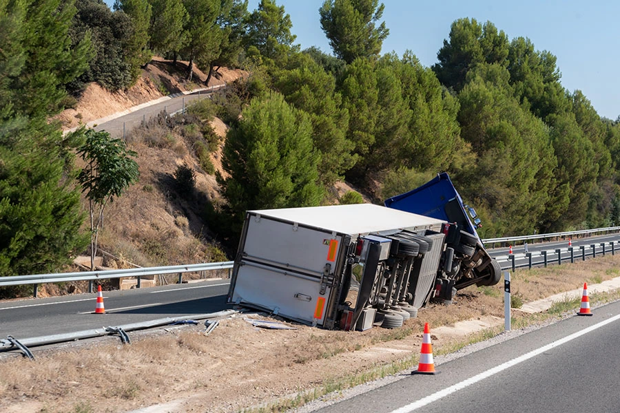 A blue and white truck overturned on its side along the guardrail of a highway.
