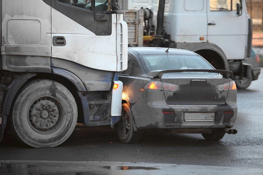 A large semi-truck colliding with the rear side of a dark sedan.