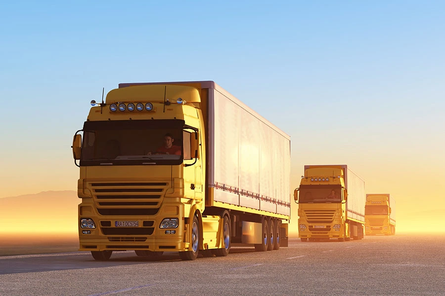 A line of yellow semi-trucks driving along a highway during sunset.