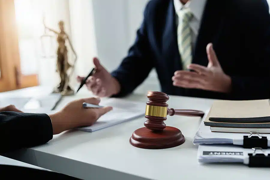 A lawyer speaking during a legal meeting with documents, a gavel, and a Lady Justice statue on the desk.