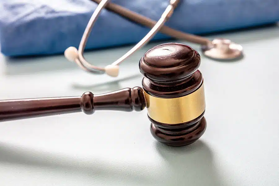 A wooden judge's gavel lying on a surface with a stethoscope in the blurred background.