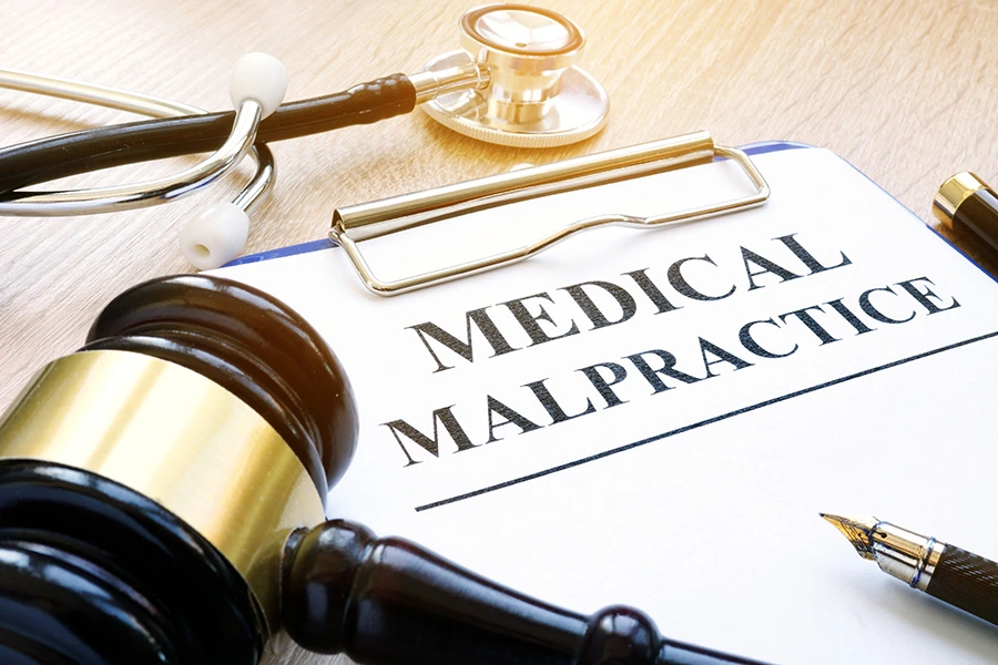 A gavel, stethoscope, and pen surrounding a clipboard labeled "MEDICAL MALPRACTICE."
