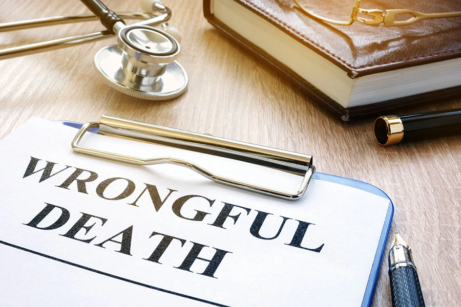 A clipboard with a document titled "WRONGFUL DEATH" resting on a wooden desk beside a stethoscope and pen.