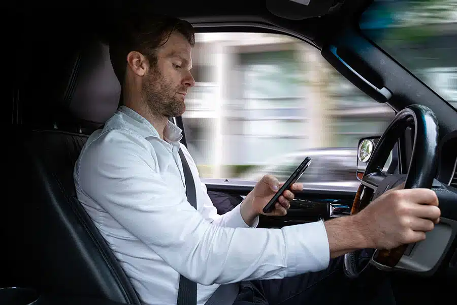 A man using his smartphone with one hand while driving a car.