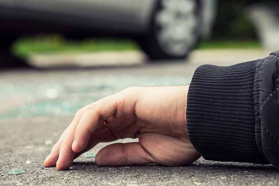 A close-up of a person's hand lying on the road amid shattered glass following a traffic accident.