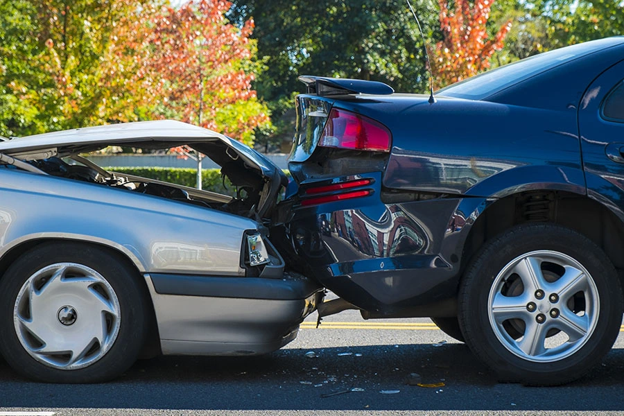 A silver car with a heavily crushed hood crashed into the rear of a dark blue sedan on a street.