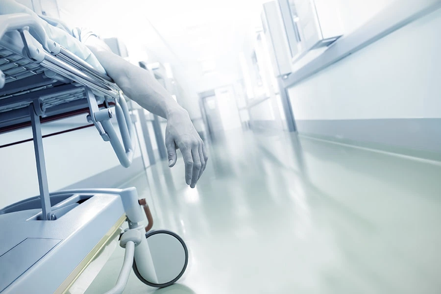 A patient's arm hanging off the side of a gurney in a hospital corridor.